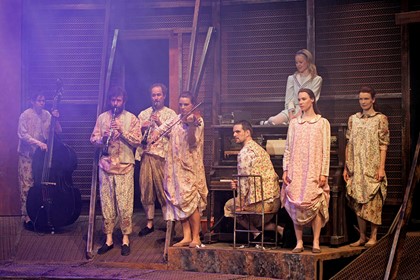 Production still for "The Odyssey". L-R: Leon Ewing, Francis Greenslade, Paul Blackwell, Jennifer Ipkendanz, Ben Lewis, Suzannah McDonald (on top of piano), Belinda McClory, Margaret Mills. Photographer: Jeff Busby